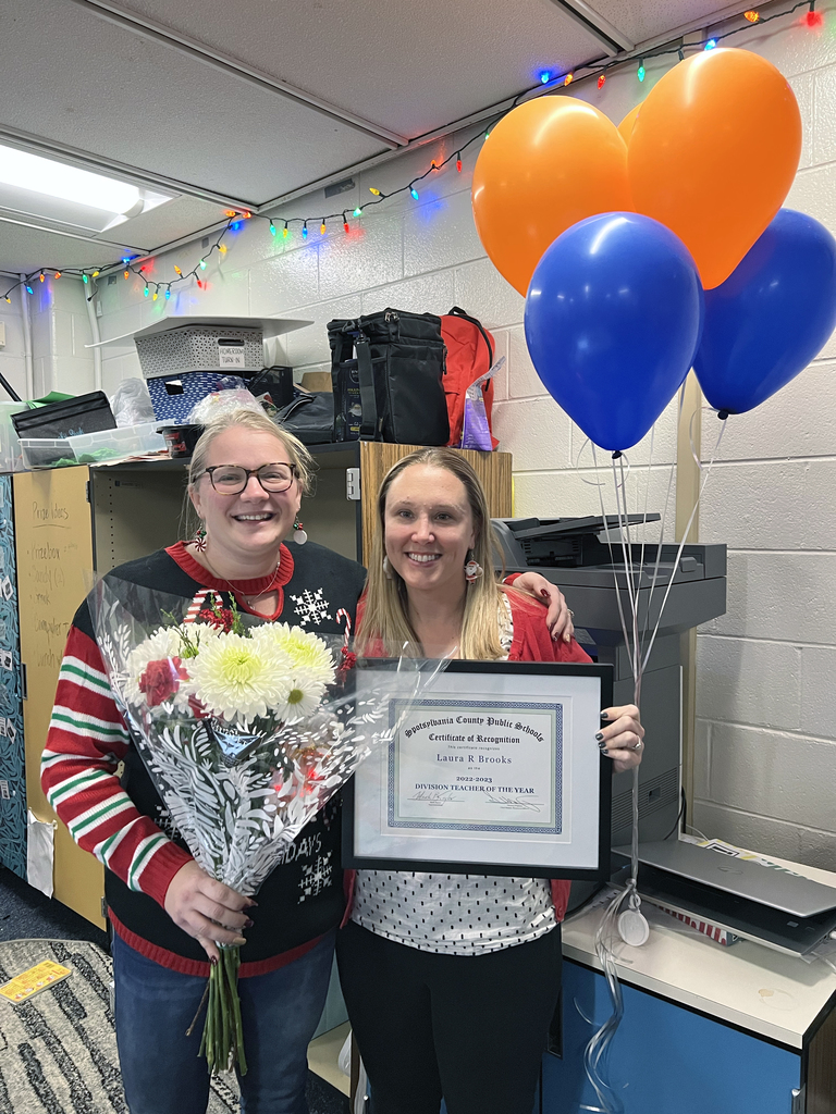Mrs. Laura Brooks holding flowers and a certificate, standing next to principal Kara Hurley with blue and orange balloons.